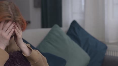 mujer estresada sosteniendo la cabeza en las manos sentada en el sofá