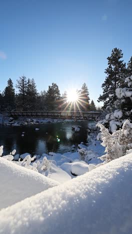 Vertical-slow-motion-dolly-of-snowy-river-with-a-bridge-illuminated-by-a-sunny-day-lens-flare