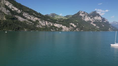 A-white-boat-yacht-float-in-calm-blue-lake-and-mountain-landscape-in-Apls-Switzerland-Swiss-alpine-village-flying-over-the-scenic-horizon-low-level-altitude-drone-shot-in-Europe-summer-tourist-season