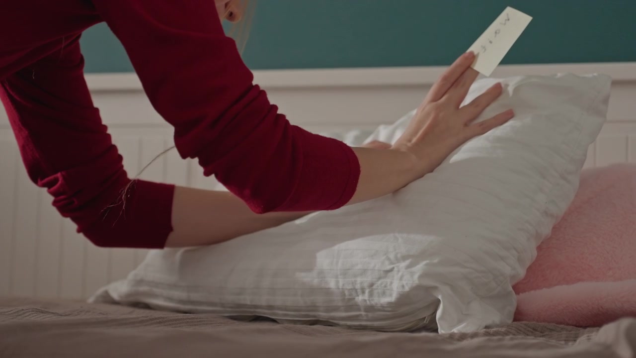 Una persona che indossa un indumento rosso a maniche lunghe interagisce. La camera da letto presenta pareti superiori color verde acqua e biancheria da letto marrone testurizzata. Un piccolo oggetto giallo poggia su un lato del grande oggetto stropicciato principale.