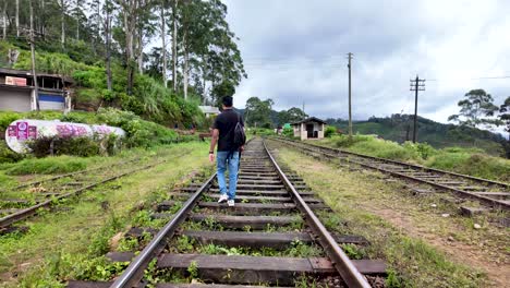 a man walks along empty railway tracks surrounded by lush greenery near the haputale-namunukula mountain range in sri lanka. the serene environment offers a sense of adventure and tranquility.