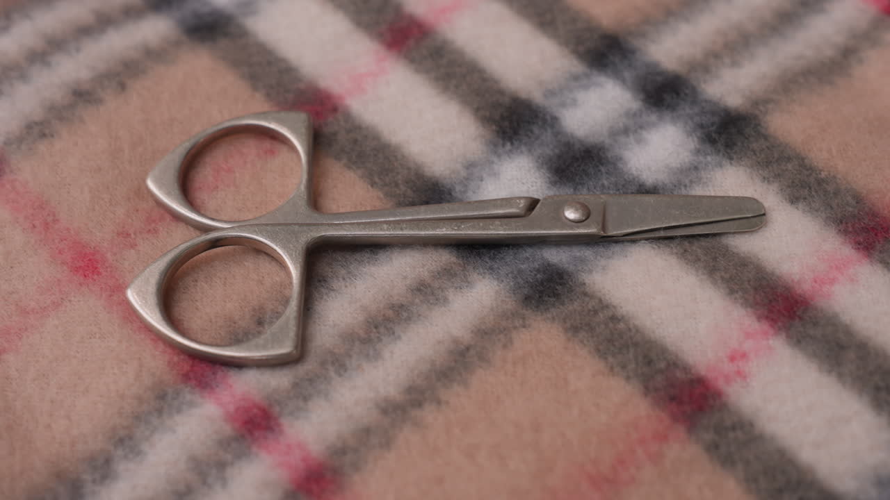 metal scissors resting on soft checkered blanket with peach embroidery thread visible, showing detailed crafting tool used in sewing, embroidery, or textile art preparation