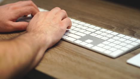 toma panorámica apretada de manos escribiendo en un teclado de computadora delgado en un escritorio de roble