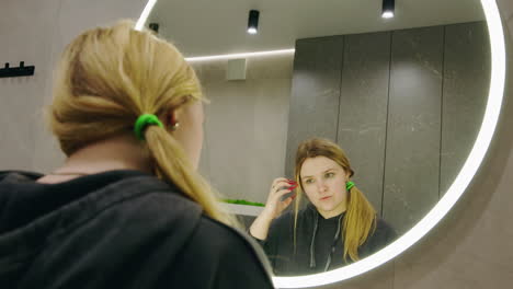 woman checking her hair in bathroom mirror