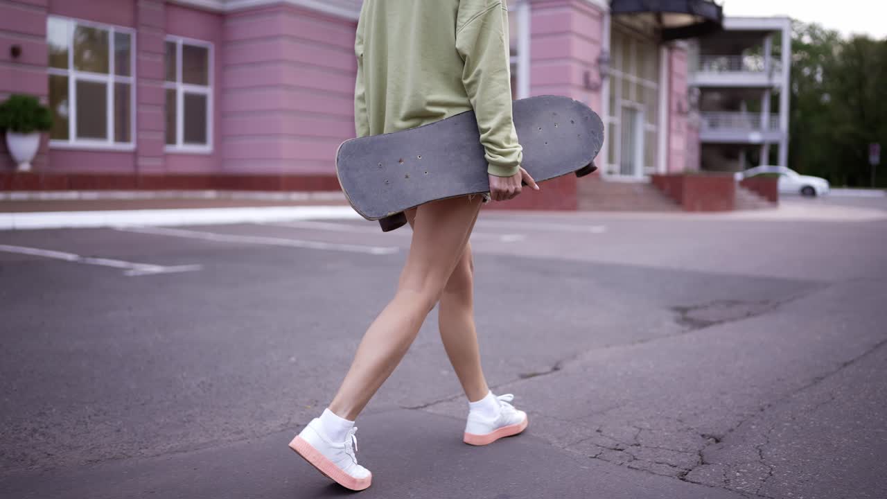 una chica camina en el parque con una patineta en sus manos, un pasatiempo diario. camina en el parque, lleva el patín a los patinadores
