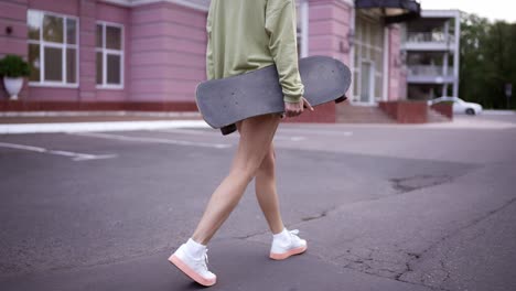 una chica camina en el parque con una patineta en sus manos, un pasatiempo diario. camina en el parque, lleva el patín a los patinadores