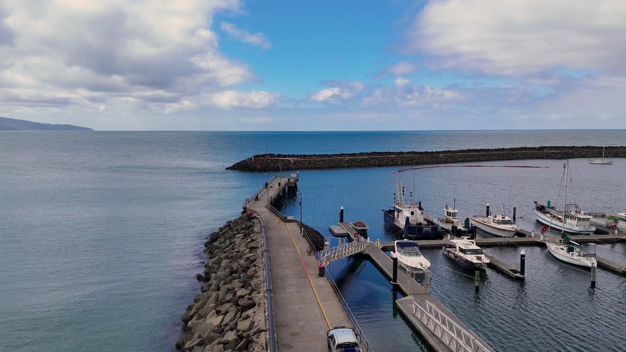 Drone captures Apollo Bay's serene harbor, showcasing boats, jetty, and rock wall under clear skies with calm waters