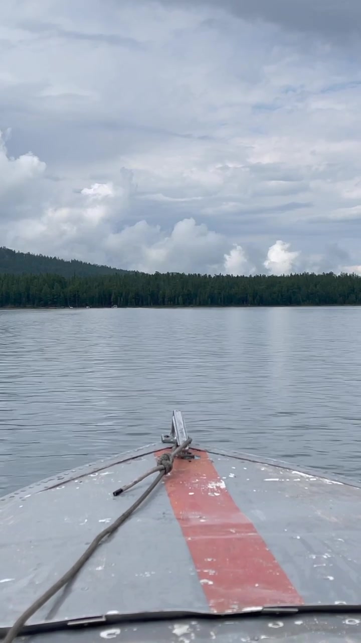 Point of view from a small boat crossing Multinsky Lakes, Altai Republic, Russia, with calm water, forested shoreline and dramatic overcast clouds in summer