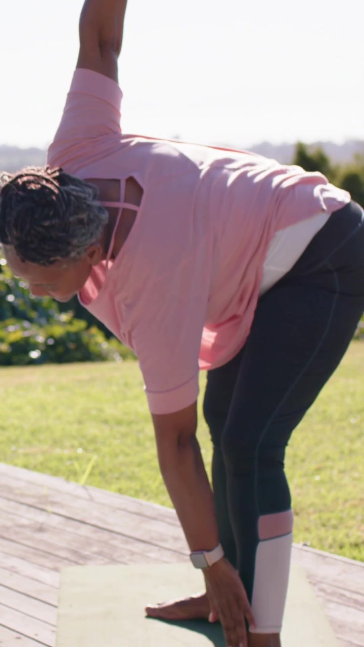 Video verticale: Reagendo a un segnale di respiro, donne con magliette rosa fanno piegamenti laterali sul ponte per l'equilibrio, con un tappetino.