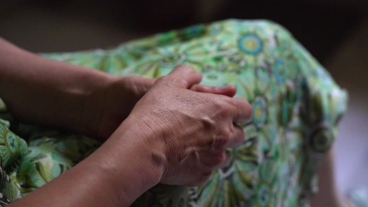 초록색 꽃 패턴의 드레스를 입은 나이 든 여성의 손이 무에 누워 있습니다.