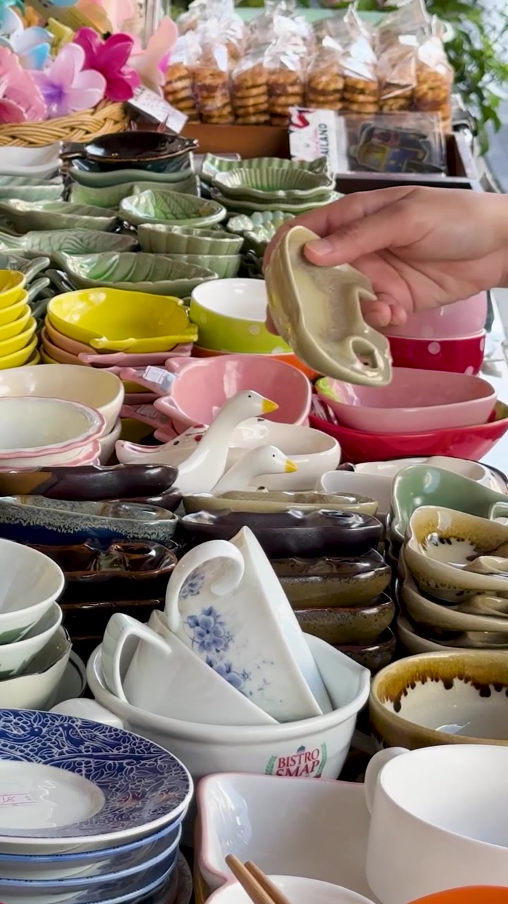 A hand browses through a colorful vertical display of handmade ceramic bowls and pottery.