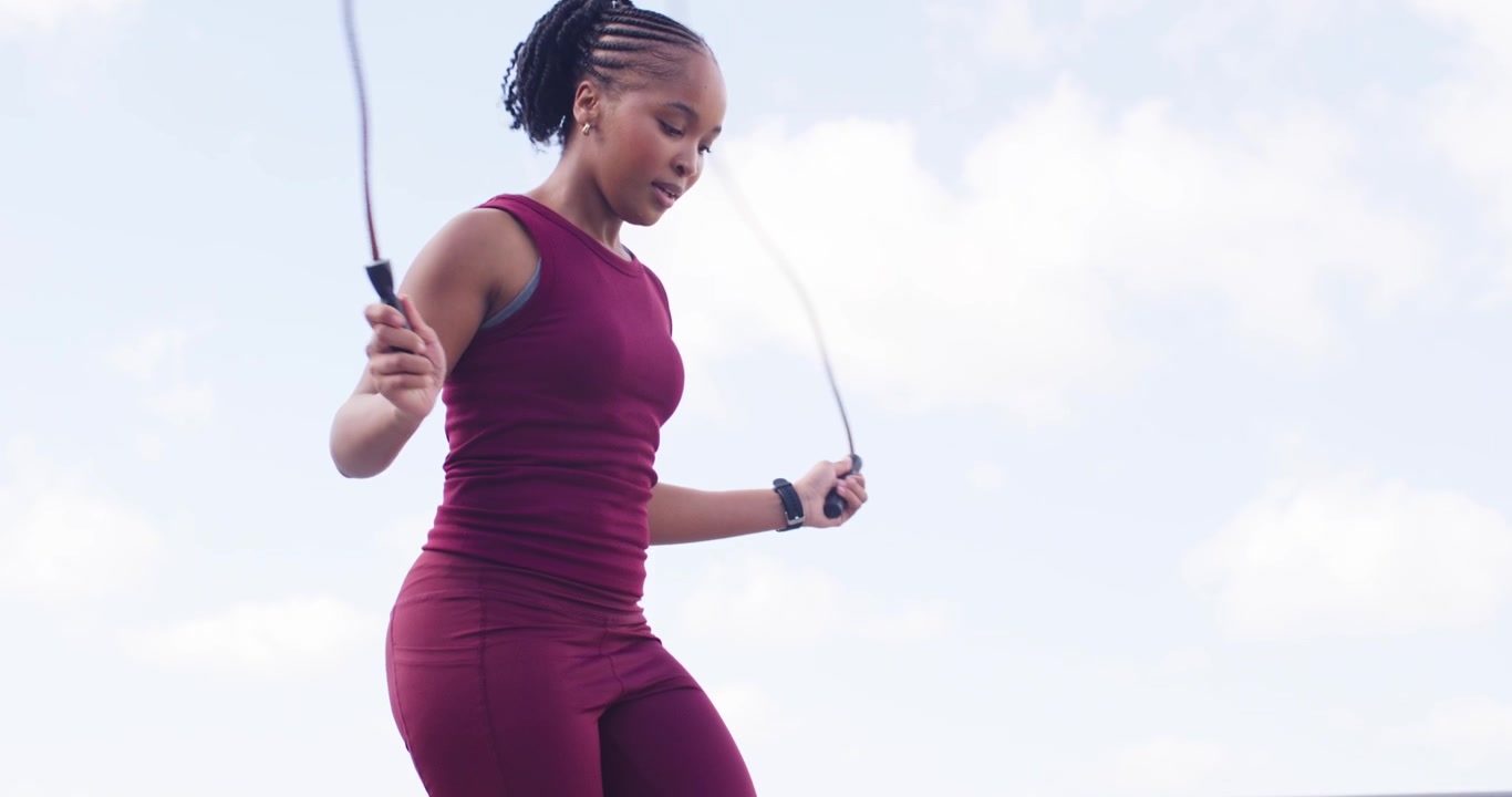 Donna africana adulta in equilibrio su una palla medica da 7 kg sul tetto, afferrando una corda e saltando per allenamento cardio