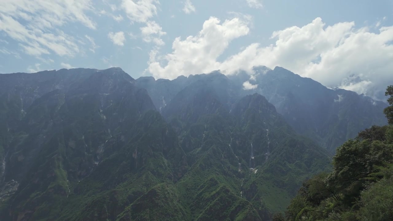 陰天白晝下，蒼翠山坡蜿蜒而下至迷霧峽谷，中國雲南西藏虎跳峽。