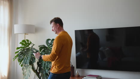 senior man in living room using smartphone, smiling near tv and houseplants, at home