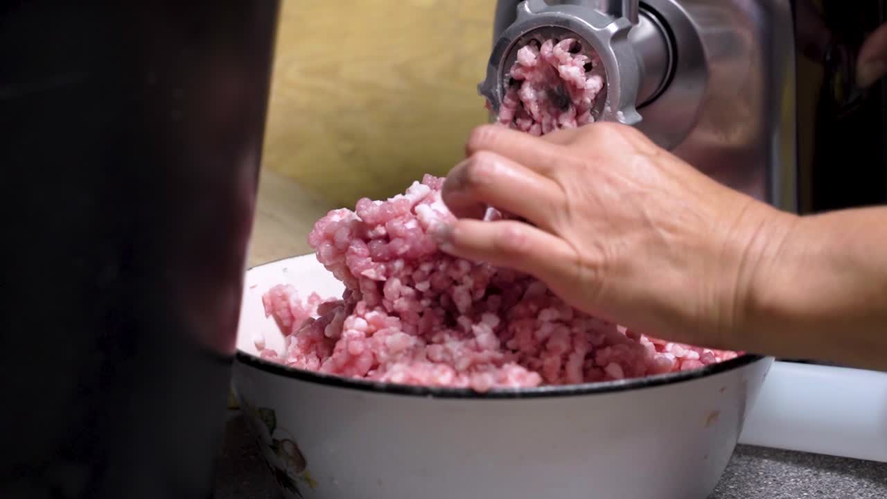 Butchers hand moving minced meat through steel cutting grinder utility in kitchen, close up