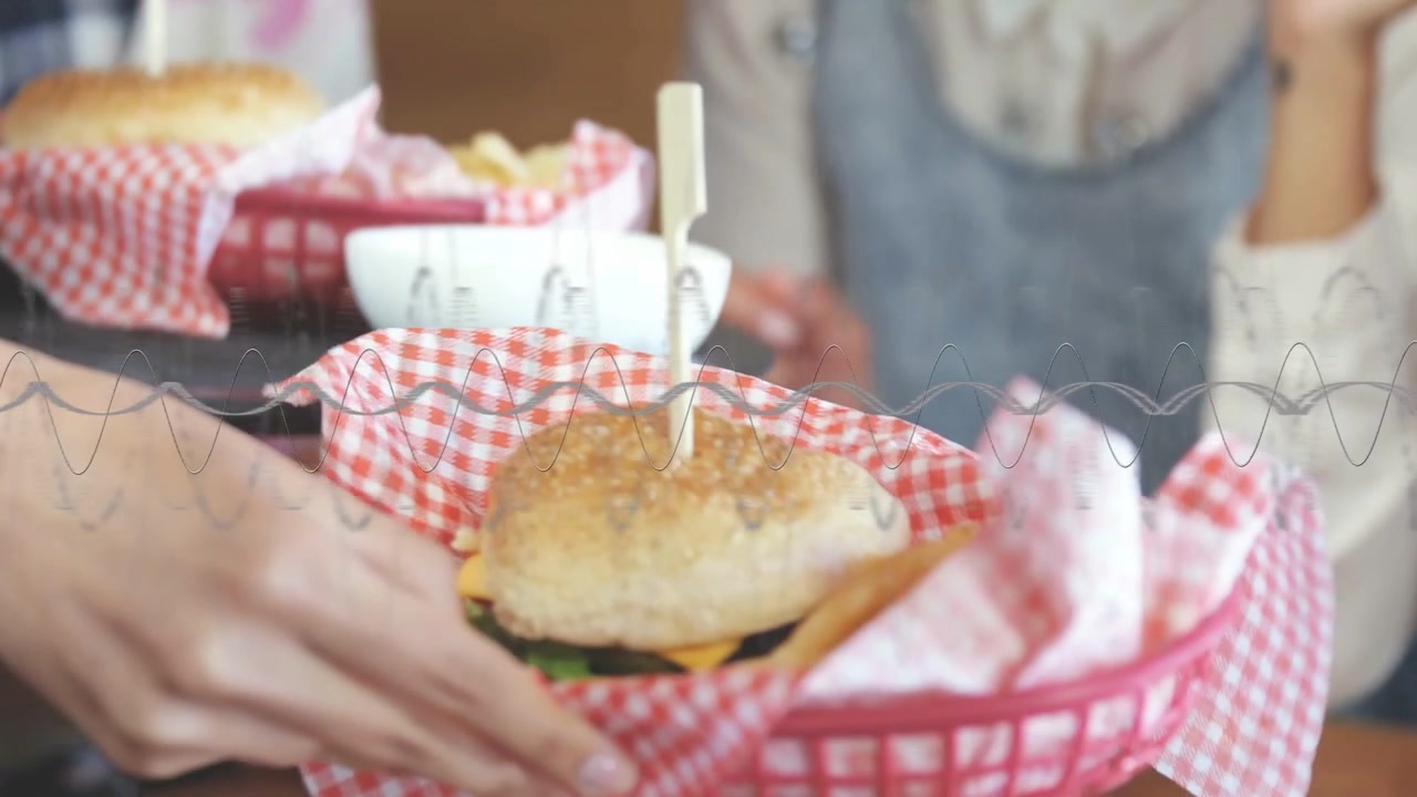 Cameriere che sposta un vassoio verso i clienti del ristorante che si allungano per prendere un cestino di hamburger su spiedini, attraverso un divisorio in vetro ondulato.