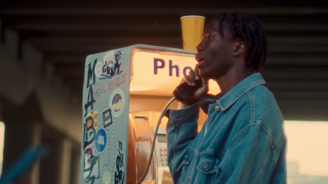 joven negro hablando en un viejo teléfono público bajo un paso elevado urbano