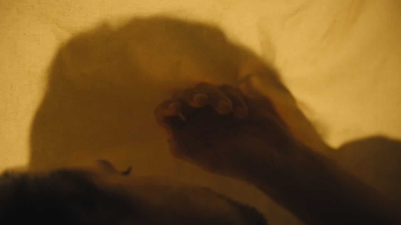 silueta de mujer retroiluminada en muselina mientras el hombre yace del otro lado