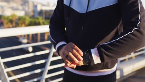 Midsection-of-african-american-man-exercising-on-footbridge-in-city,-checking-smartwatch