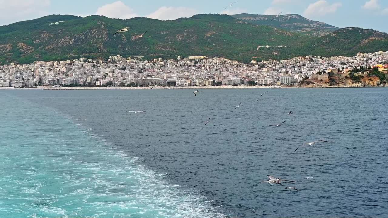 Flying seagulls near the floating ferryboat. Land in the distance. Cloudy weather. Slow motion. Greece