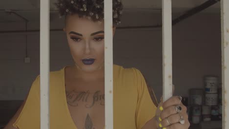 Attractive-young-woman-with-expressive-makeup-and-tattoos-holding-bars-behind-which-she-is-closed