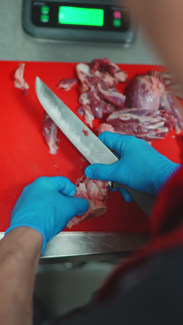Close-Up of Butcher's Hands in Blue Gloves Cutting Raw Meat