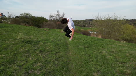 Aerial-View-of-Young-Man-Running-and-Doing-Somersault-in-Green-Outdoor-Field,-Slow-Motion