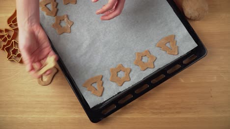 placing various christmas gingerbread shapes on a baking tin on brown wooden table topdown video