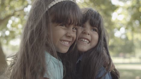 retrato cerrado de niñas latinas abrazándose, sonriendo y besándose en el parque