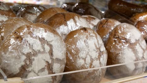 close-up of many beautiful packaged rye loafs on a wooden counter and a male hand takes one