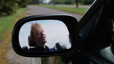 Teen-talking-while-driving-a-convertible-through-village-road-in-side-mirror