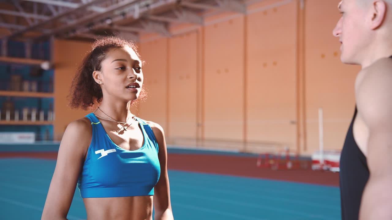 joven deportista hablando con deportista en una instalación deportiva cubierta durante la sesión de entrenamiento