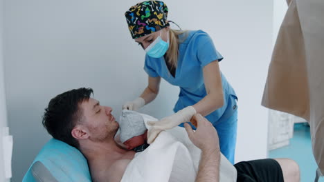 tiny newborn is put on the bare chest of a father. nurse is helping to cover the baby with sheets and blankets.
