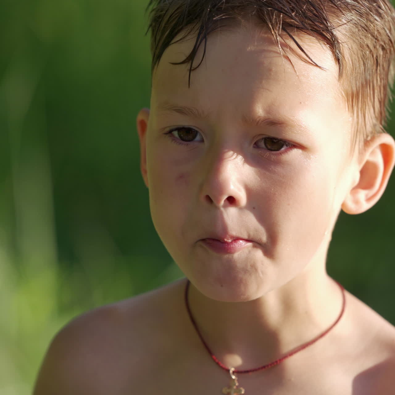 Portrait of a cute hungry boy outdoors. Little boy with wet hair is eating something on blurred background in summer.