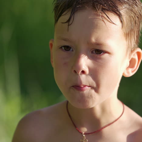 portrait of a cute hungry boy outdoors. little boy with wet hair is eating something on blurred background in summer.