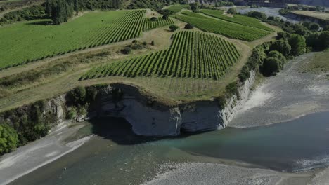 drone pulls back to reveal cliffside vineyard next to a river in marlborough new zealand