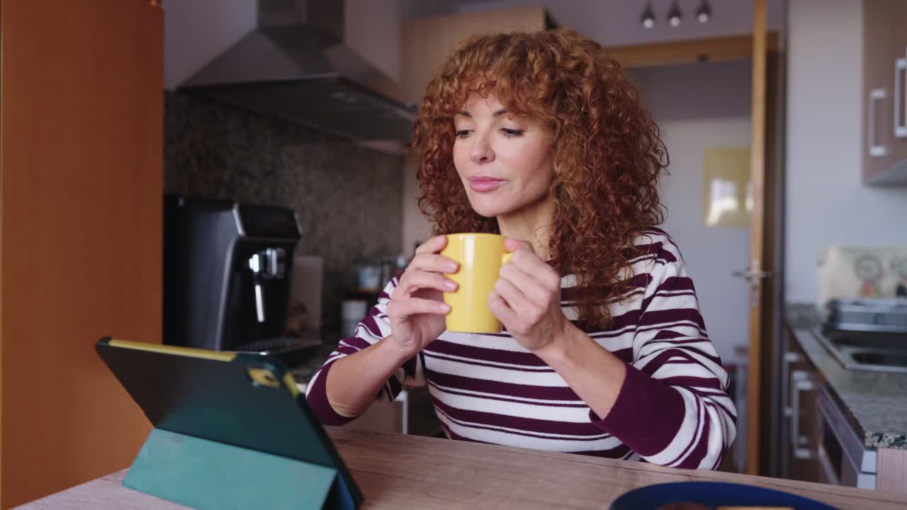 Donna che beve caffè e usa il tablet in cucina