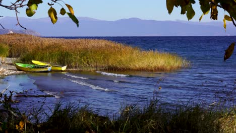 bahía del lago con barcos de pesca anclados cerca de juncos marrones en un día ventoso y soleado de otoño