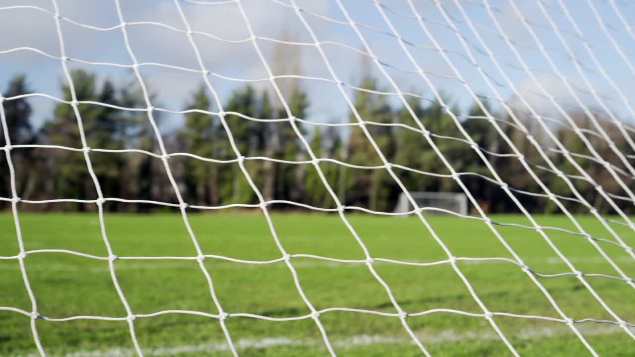 Soccer net foreground with green grass and blue sky pan to right