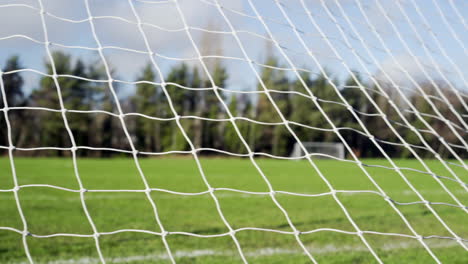 soccer net foreground with green grass and blue sky pan to right