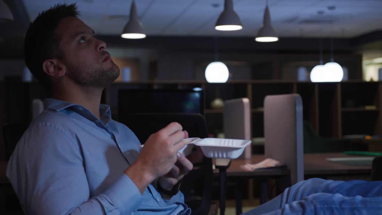Businessman eating in a modern office by night