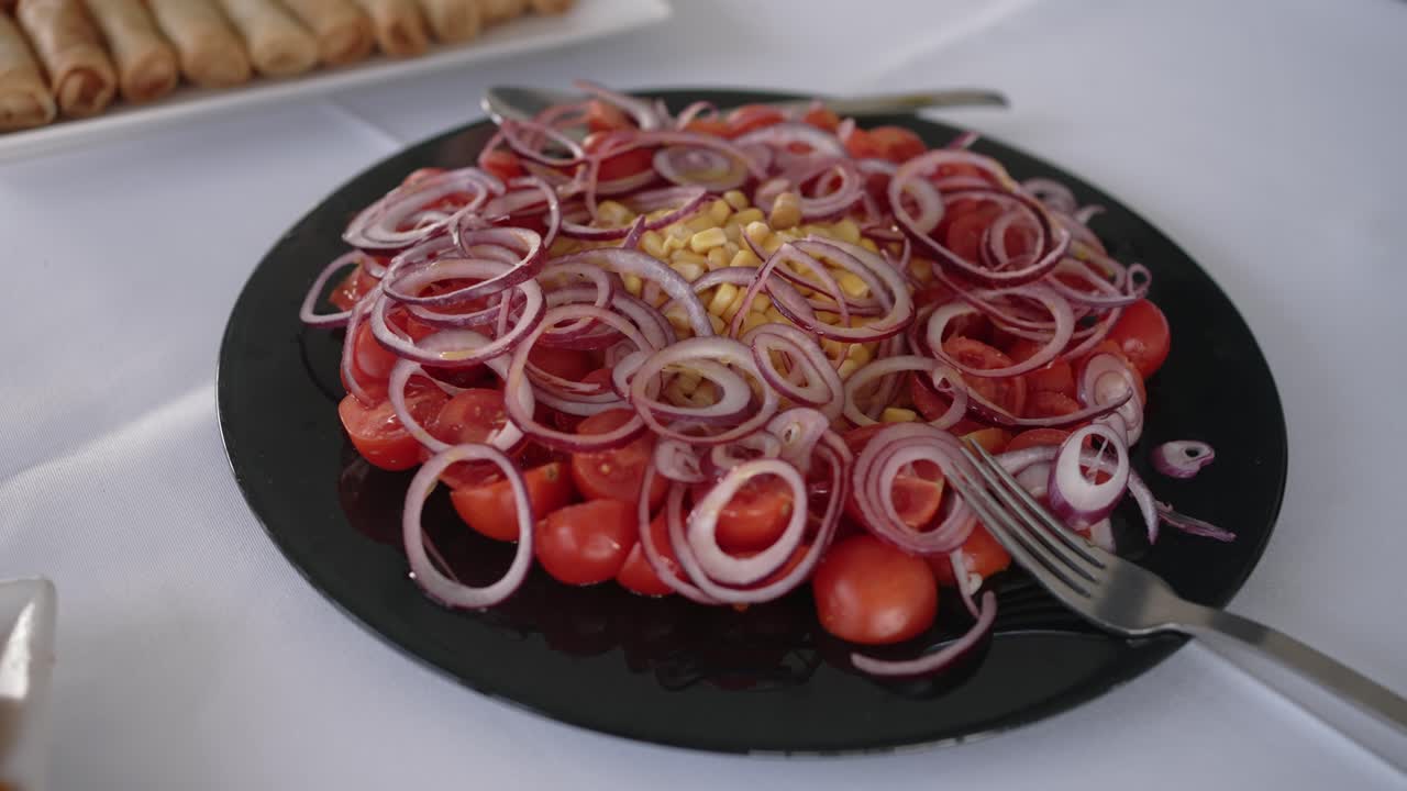 Tomato salad with red onion rings and corn served on a black plate during a festive meal