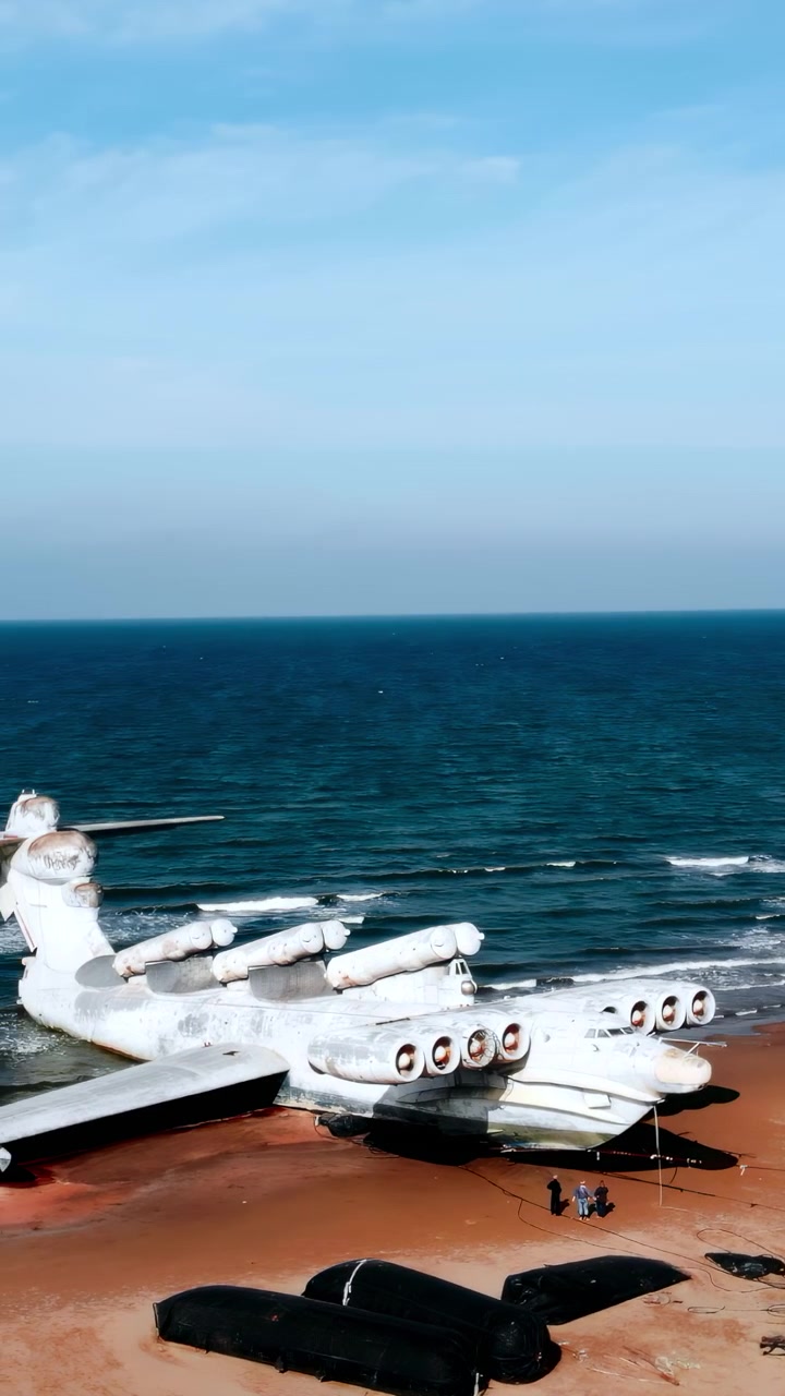 Macchinari pesanti che rimuovono la sabbia intorno a un aereo arenato, escavatore e piattaforma che preparano il recupero, gommone nero. Media