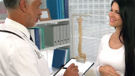 médico escribiendo y hablando con una mujer embarazada