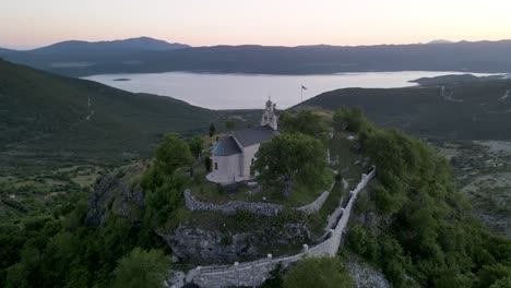 Hilltop-church-against-beautiful-lake-at-sunset,-Montenegro
