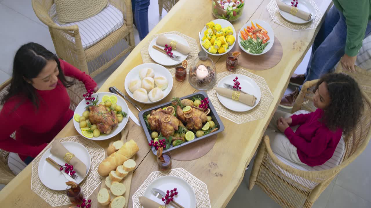 Father gesturing inviting family gathering at wooden table placing salad and rolls holding hands