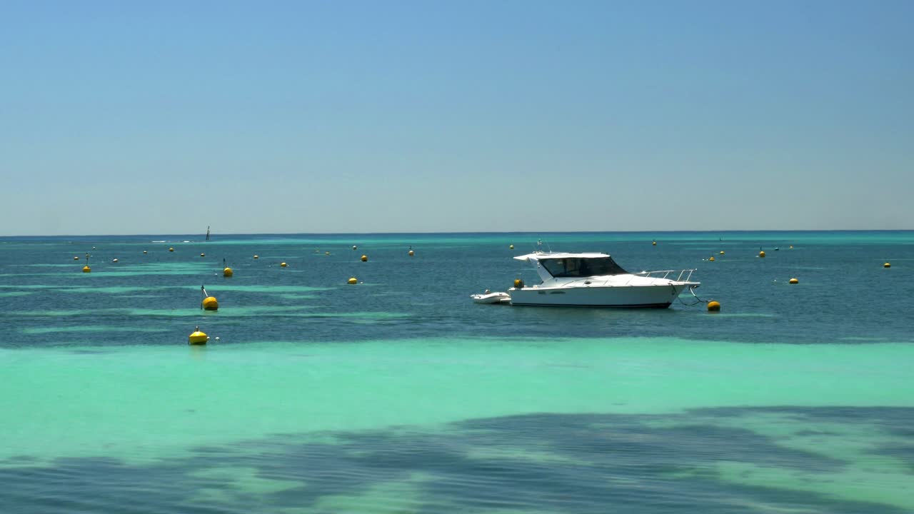 Yacht sits in crystal-clear waters near buoys and birds