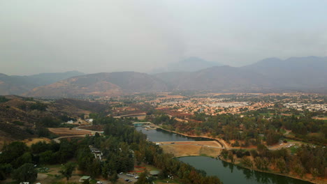 aerial view of a valley with a lake, mountains, and a distant town under a hazy sky