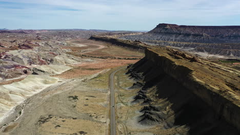 Aerial-view-overlooking-a-car-driving-on-a-scenic-desert-road-in-southwest-USA