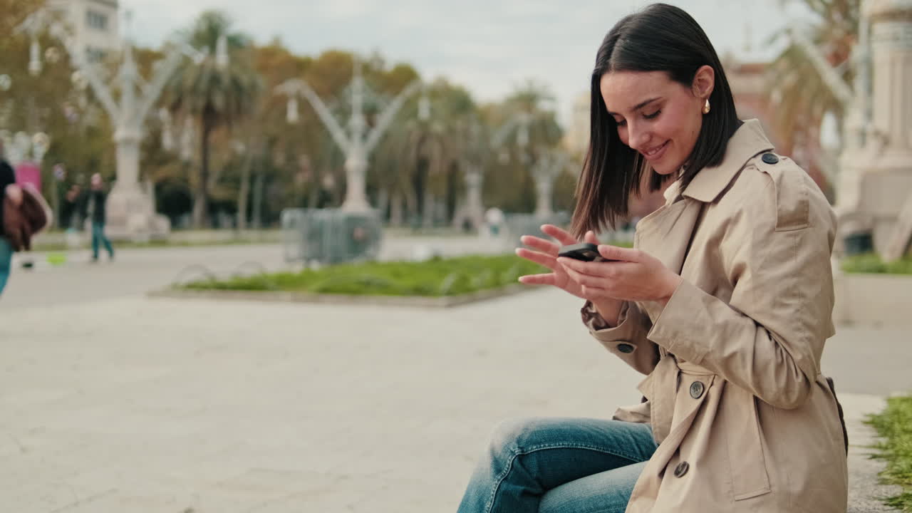 Joven mujer sonriente usando el smartphone mientras está sentada en un parque de la ciudad
